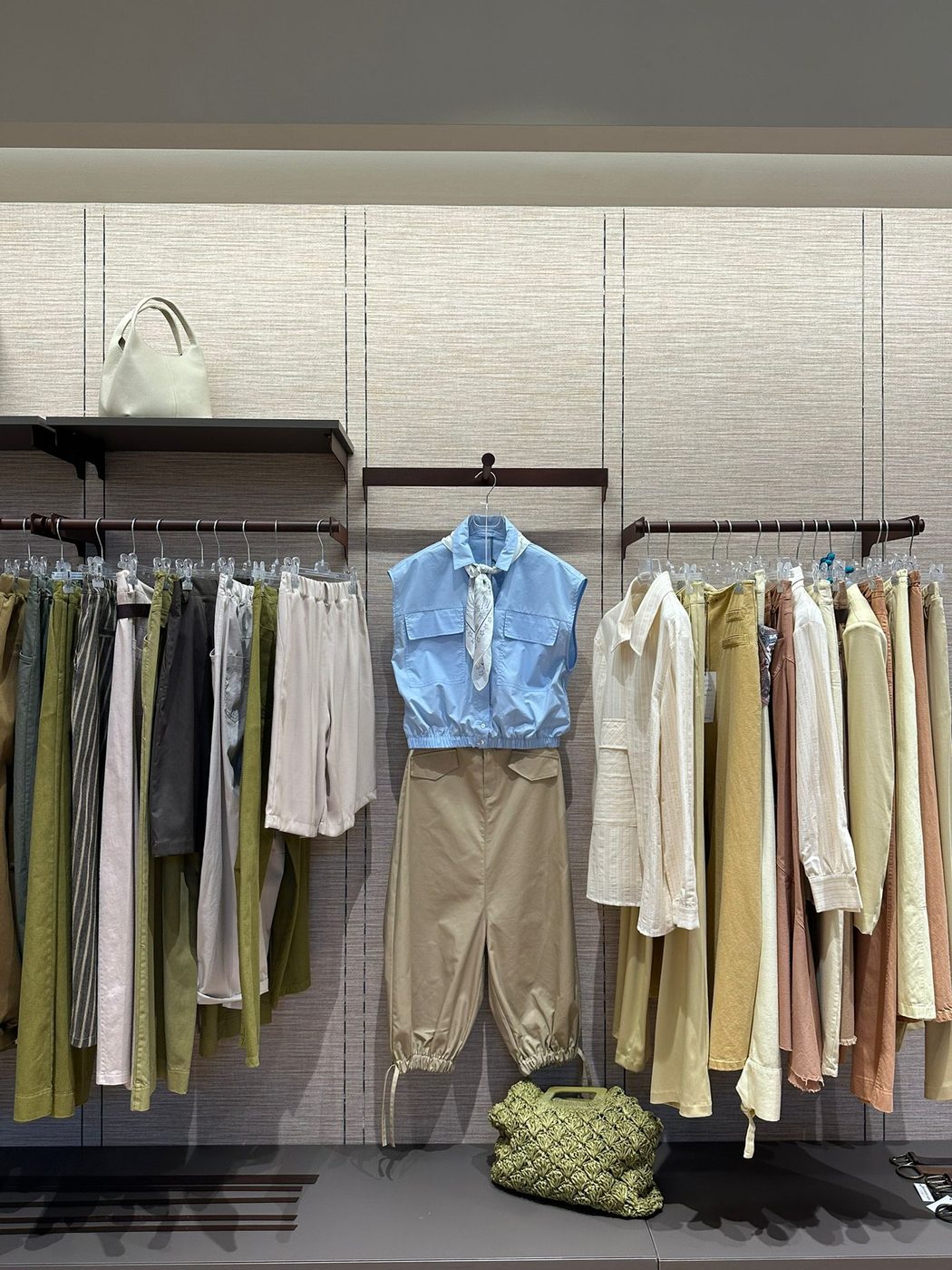 Parete dello showroom Queen Fashion — selezione stagionale di pantaloni in toni terra, verde oliva e pastello